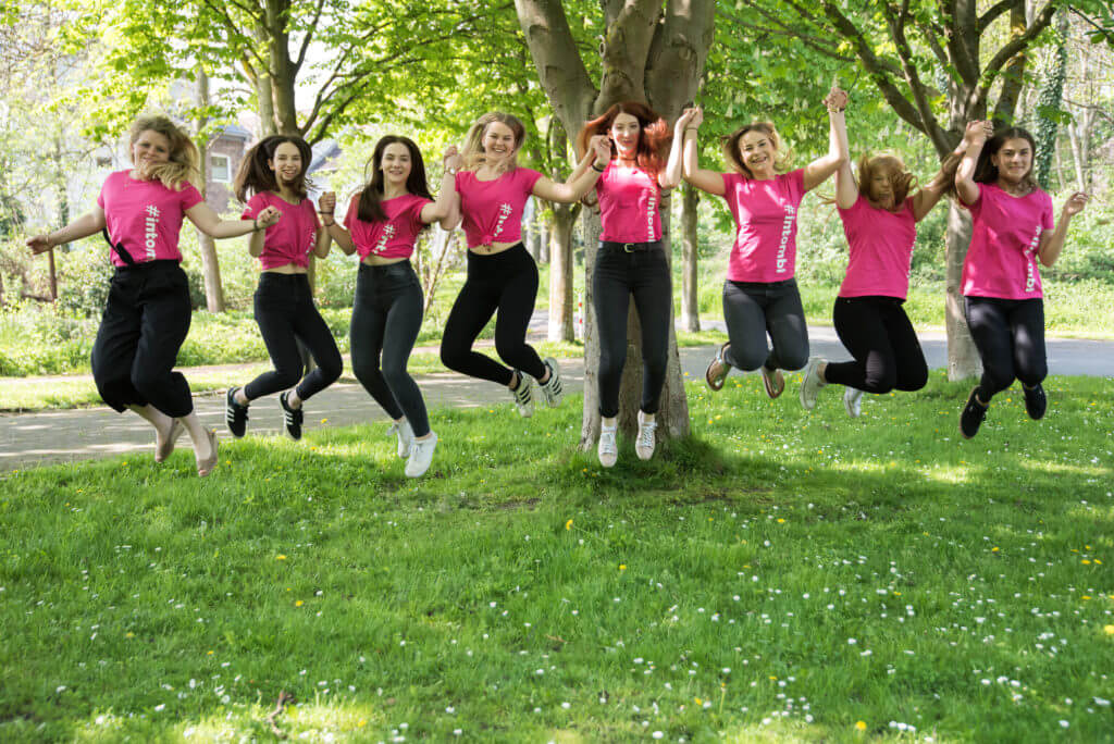 Acht Mädchen und junge Frauen halten sich an den Händen und springen gemeinsam in die Luft