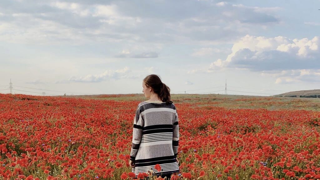 Eine Frau steht mit dem Rücken zu Kamera und blickt in ein rotes Blumenfeld