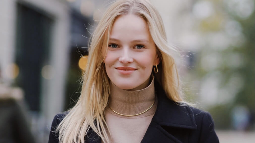 Vivien is wearing a beige pullover with a turtleneck and over that a black jacket. She is smiling in the camera.