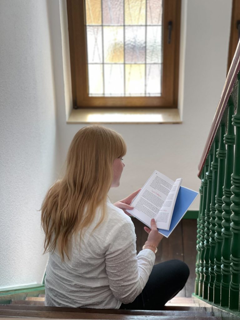 Lisa, aus dem intombi Team, sitzt auf der Treppe und liest Mädchensache, das neue Buch von Sina Oberle. 